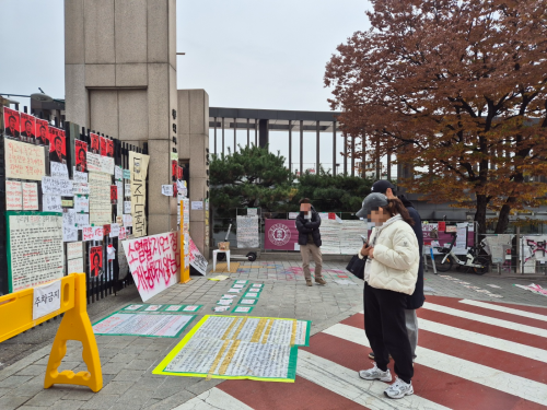 신남성연대의 ‘동덕여대 공학 전환 환영 및 페미니즘 규탄 집회’가 취소된 지난 20일 정오쯤 서울 성북구 동덕여대 앞을 지나가던 시민들이 학생들이 바닥에 붙인 대자보를 읽어보고 있다. 송현주 기자