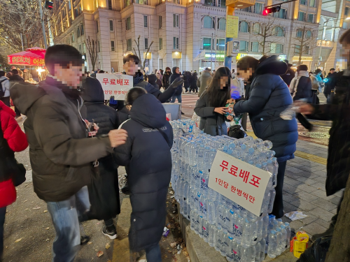 지난 7일 오후 서울 영등포구 국회 앞 윤석열 대통령 탄핵 촉구 집회에 참석한 한 남성이 초등학생 딸과 함께 시민들에게 무료로 생수를 나눠주고 있다. 김우진 기자