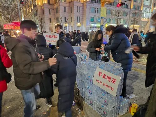 지난 7일 오후 서울 영등포구 국회 앞 윤석열 대통령 탄핵 촉구 집회에 참석한 한 남성이 초등학생 딸과 함께 시민들에게 무료로 생수를 나눠주고 있다. 김우진 기자