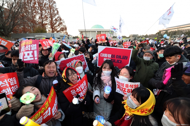 윤석열 대통령 탄핵소추안이 가결된 지난 14일 서울 여의도 국회의사당 앞에 모인 시민들이 ‘윤석열을 탄핵하라’ 등의 피켓을 든 채 환호하고 있다.