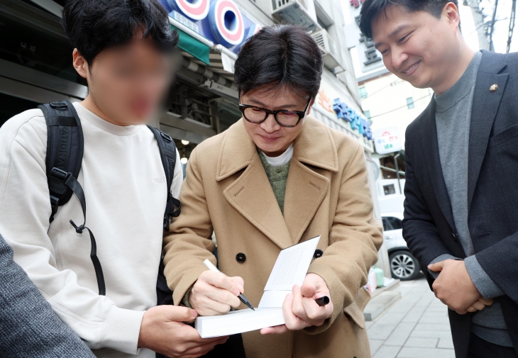 약 두 달 반 만에 공개 행보에 나선 한동훈(가운데) 전 국민의힘 대표가 2일 서울 종로구 대학로에서 ﻿자신의 저서 ‘국민이 먼저입니다’를 들고 있는 지지자에게 사인을 해 주고 있다. 연합뉴스