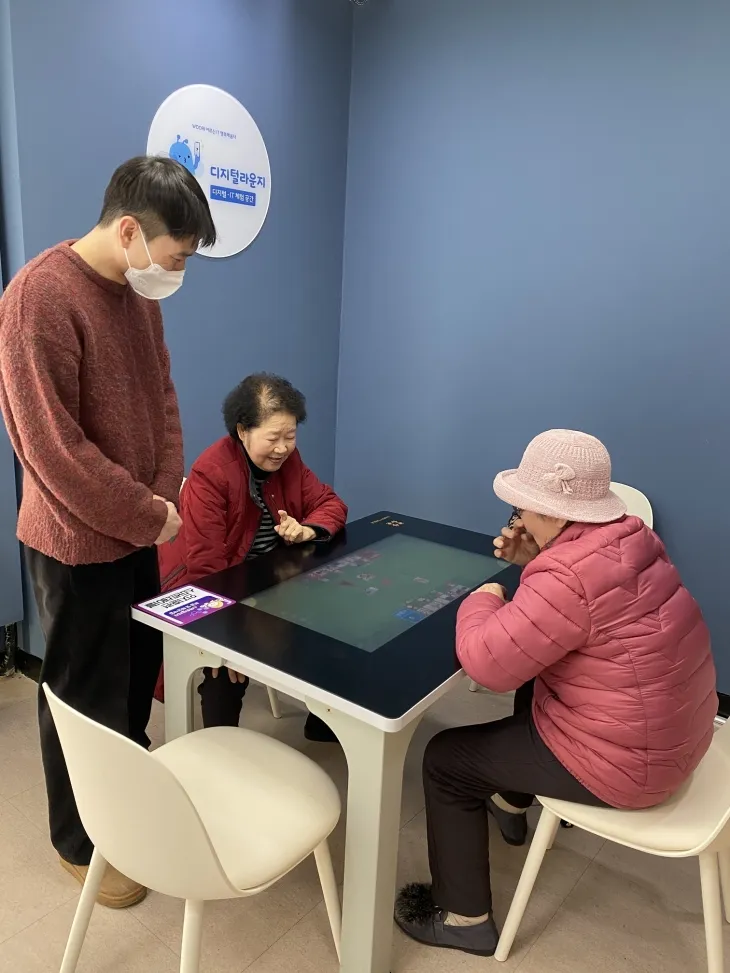 디지털 라운지에서 어르신들이 스마트 테이블을 활용해 디지털 체험을 하고 있다. 담당자가 어르신들의 학습을 돕고 있다.