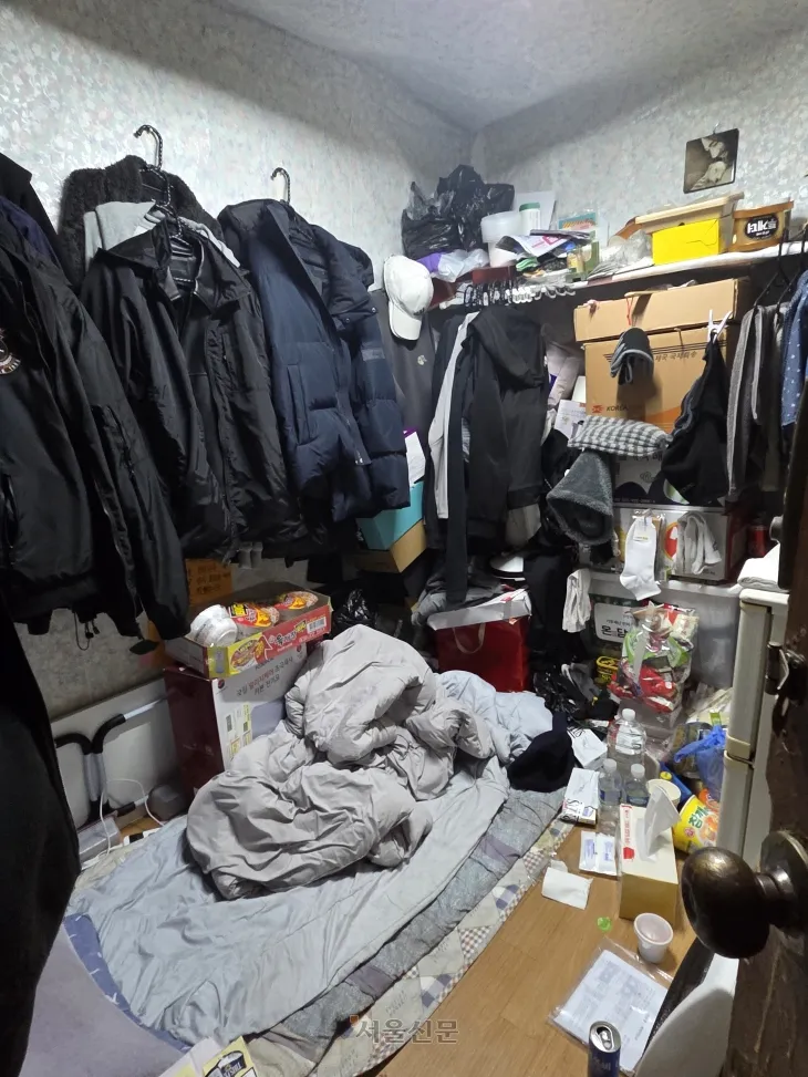비좁은 쪽방에 겨울 외투와 생필품, 식료품이 뒤섞여 있는 모습.