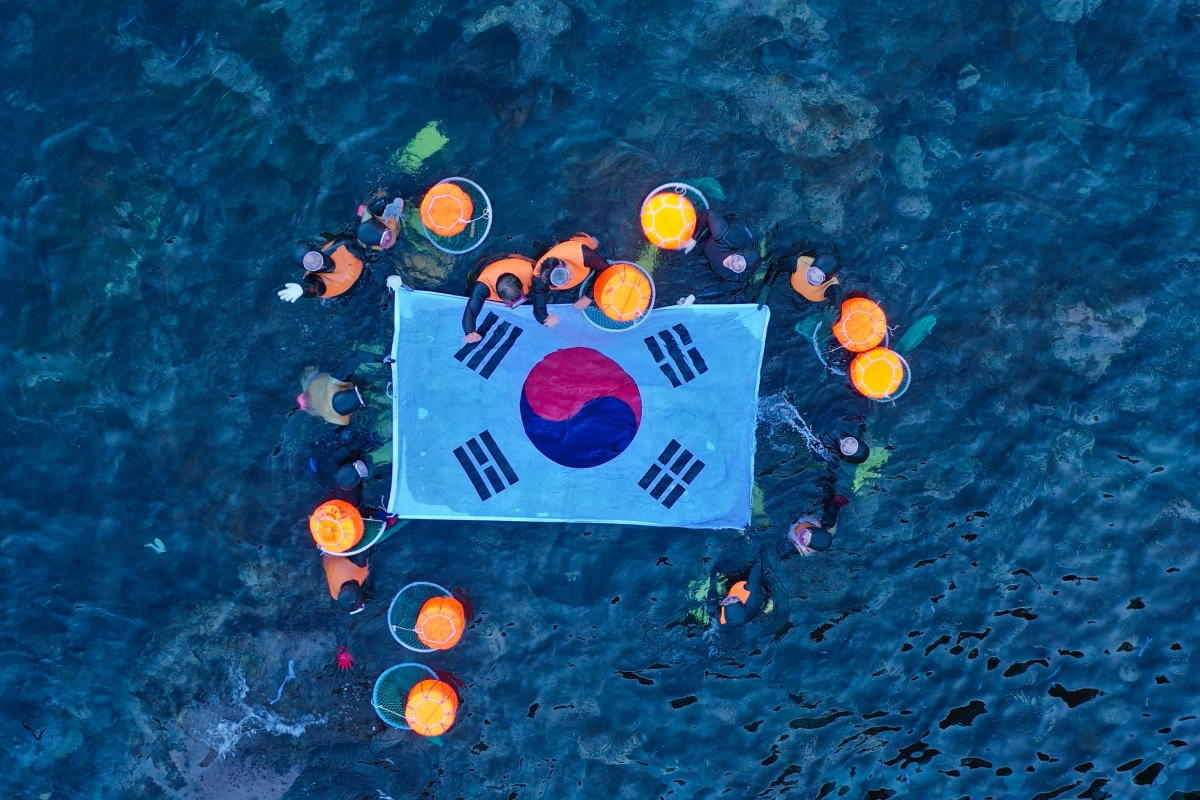 8일 독도 몽돌해안에서 제주해녀와 울릉해녀들이 합동 물질을 한 뒤 바다위에 태극기를 펼쳐들고 있다. 제주도 제공