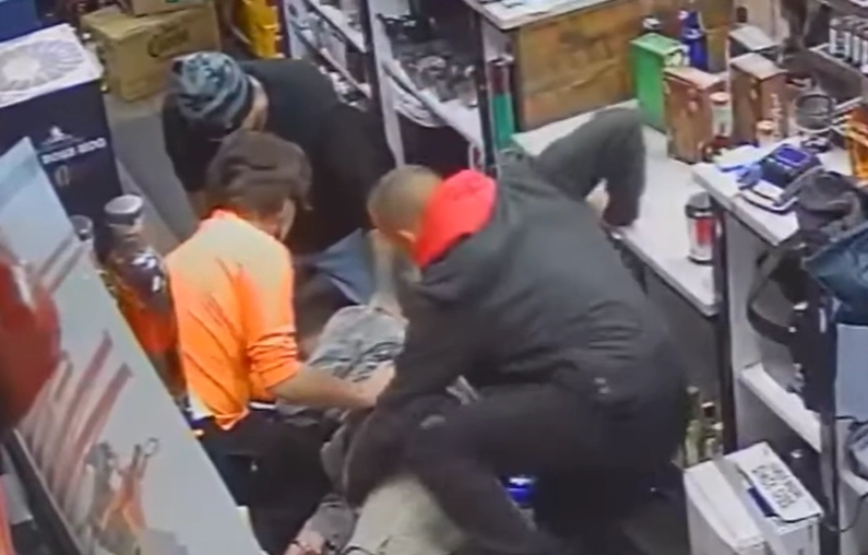 빨간색 후드티를 입은 한 남성이 심장마비로 쓰러진 주류 판매점 직원을 돕는 척 그의 몸을 더듬고 있다. 유튜브 채널 ‘KPTV 폭스12’ 캡처