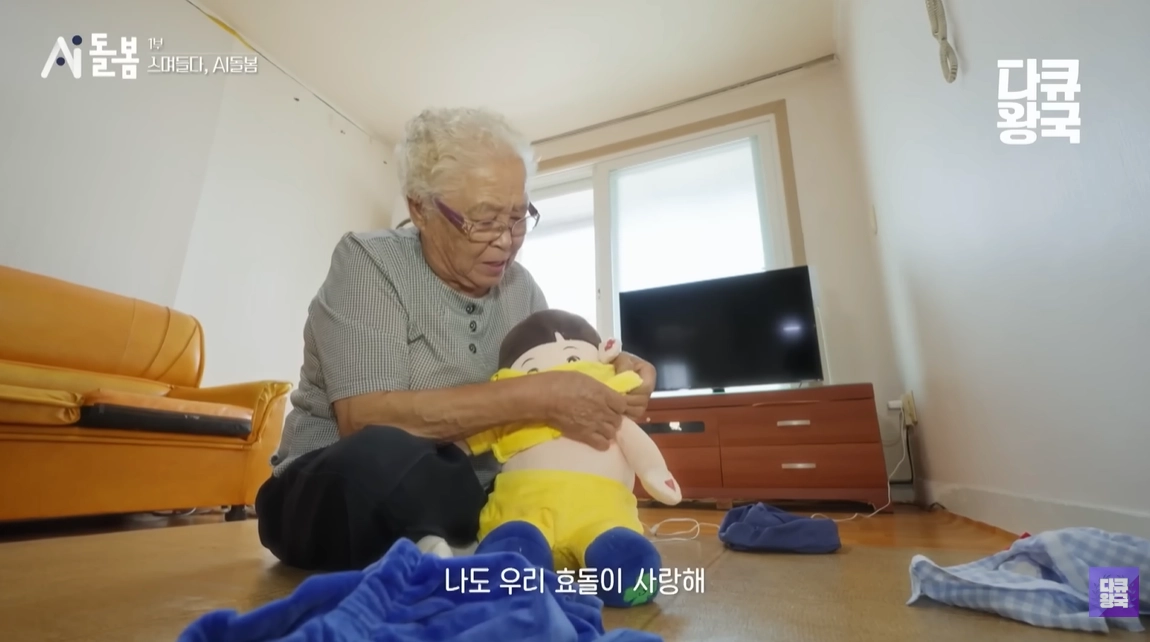 지난해 11월 MBC충북에서 방송된 특별기획 ‘ AI 돌봄’ 1부 ‘스며들다: AI 돌봄’에서 이희수 할머니가 인공지능(AI) 돌봄 로봇 효돌에게 시장에서 사온 옷을 입혀주고 있다. 유튜브 채널 ‘다큐왕국’ 캡처