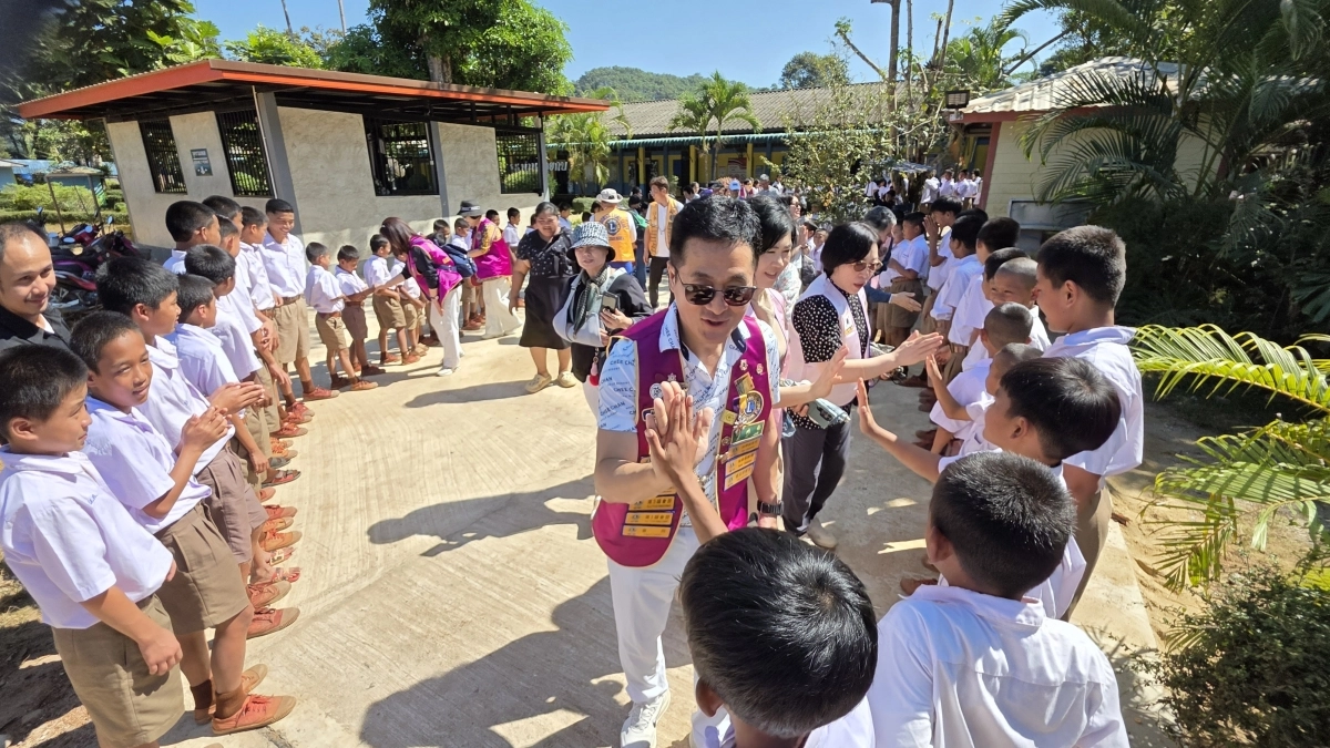 국제라이온스협회 354-D지구 회원 30명이 교내 도로 포장공사 후 준공식에 참석하기 위해 태국 깐짜나부리 서북부지역에 있는 아리랑초등학교에 들어서고 있다. 이기환(58) 회원  등이 “안녕하세요”라고 인사하는 학생들과 악수하거나, 하이파이브를 하고 있다.