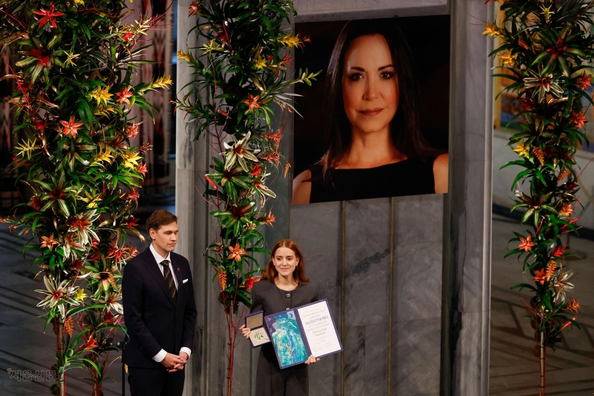 베네수엘라 야권 지도자 마리아 코리나 마차도의 사진이 걸린 노르웨이 오슬로 시청에서 10일(현지시간) 열린 노벨평화상 시상식에서 딸 아나 코리나 소사(오른쪽)가 어머니를 대신해 상을 수상하고 있다.   오슬로 AFP 연합뉴스