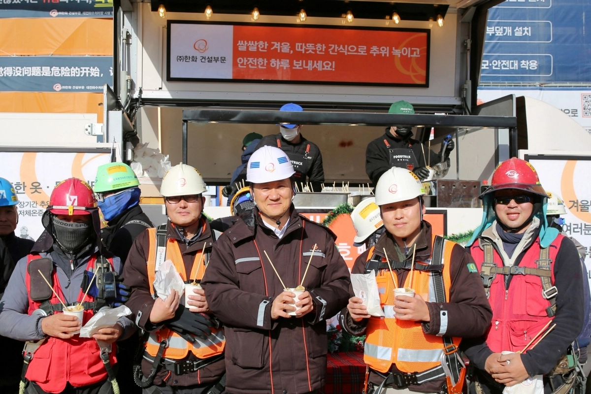 김우석(왼쪽 세 번째)한화 건설부문 대표이사가 건설현장 근로자들과 함께 ‘찾아가는 겨울간식차’의 호빵과 어묵을 즐기며 기념 촬영을 하고 있다. 한화 건설부문 제공