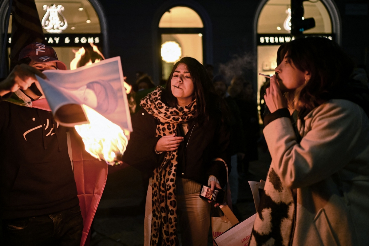 밀라노 미국 영사관 밖에서 반이란 정권 시위대가 이란 최고 지도자 알리 하메네이의 모습을 담은 불붙은 종이로 담배에 불을 붙이고 있다. 2026.1.14 AFP 연합뉴스