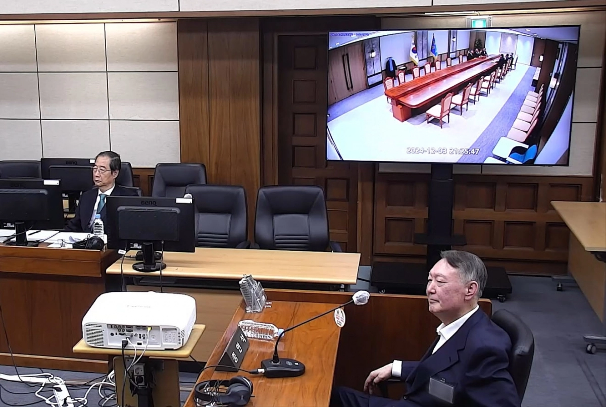 윤석열(오른쪽) 전 대통령이 지난해 11월 19일 서울 서초구 서울중앙지법에서 열린 한덕수(위쪽) 전 국무총리의 내란 중요임무 종사 등 혐의 공판에 증인으로 출석해 앉아 있다. 벽면 모니터에는 12·3 비상계엄 전 국무회의 당시의 회의실 폐쇄회로(CC)TV 영상이 띄워져 있다. 서울중앙지방법원 제공