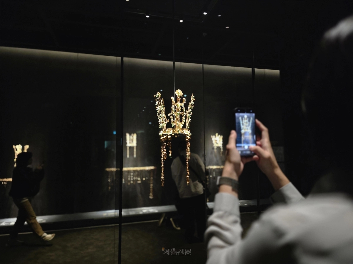 국립경주박물관이 2025 아시아태평양경제협력체(APEC) 정상회의를 기념해 특별전 ‘신라 금관, 권력과 위신’을 여는 가운데 지난해 10월 박물관 관계자가 국보인 황남대총 북분 금관을 휴대전화 카메라에 담고 있다. 황남대총 북분 금관 뒤로 금령총, 금관총, 서봉총 금관이 보인다. 경주 윤수경 기자