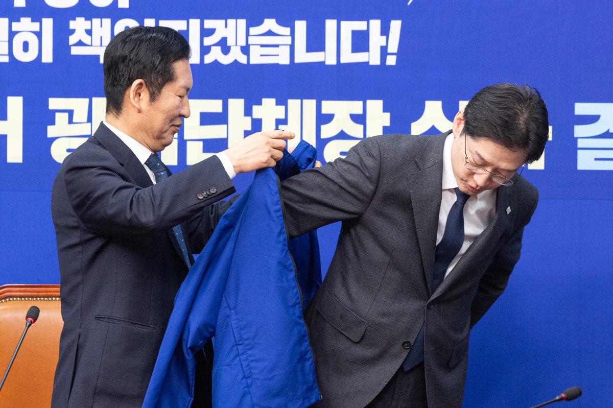 5일 서울 여의도 국회에서 열린 더불어민주당 공천 심사 결과 발표에서 정청래 대표가 경남지사 후보로 단수 공천된 김경수 지방시대위원장에게 파란색 점퍼를 입혀주고 있다. 2026.3.5 뉴스1