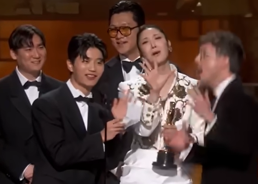 넷플릭스 애니메이션 영화 ‘케이팝 데몬 헌터스’의 주제곡 ‘골든’을 작곡한 더 블랙 레이블 소속 프로듀서 팀 아이디오(IDO)와 작곡가 24, ‘골든’을 작곡하고 직접 부른 이재(EJAE), 마크 소넨블릭이 15일(현지시간) 미 로스앤젤레스 돌비 극장에서 열린 제98회 아카데미 시상식에서 주제가상을 받은 뒤 무대 위에 올랐다. IDO의 일원인 이유한이 수상소감을 발표하는 도중 퇴장을 재촉하는 음악이 흘러나오자 이재가 당혹스런 표정으로 손짓을 하고 있다. 2026.3.15 로스앤젤레스 AP 뉴시스