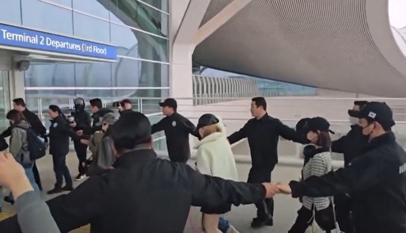 18일 인천국제공항에서 SM엔터테인먼트 소속 걸그룹 ‘하츠투하츠’가 공항 게이트에 들어가려 하자 경비업체 직원들이 ‘인간띠’를 만들어 멤버들을 에워쌌다. 자료 : 온라인 커뮤니티