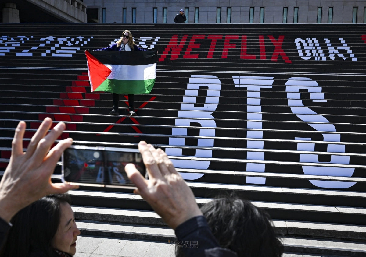 방탄소년단(BTS) 광화문 공연을 이틀 앞둔 19일 서울 종로구 세종문화회관 계단에서 한 외국인 관광객이 BTS 문구를 배경으로 팔레스타인 국기를 든 채 기념촬영을 하고 있다. 2026.3.19 이지훈 기자