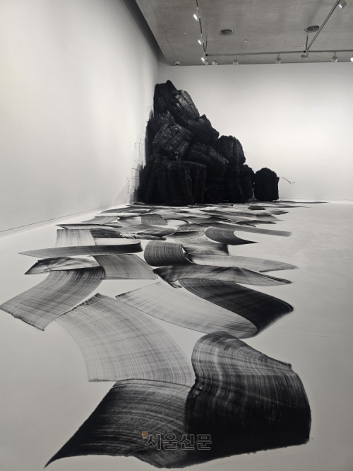 ‘숯의 작가’ 이배가 강원 원주시 뮤지엄 산에서 개인전을 여는 가운데 참나무, 버드나무 등 여러 종류의 나무로 만든 숯으로 바닥 그림을 그리고 숯 더미를 함께 설치해 만든 작품이 놓여 있다.