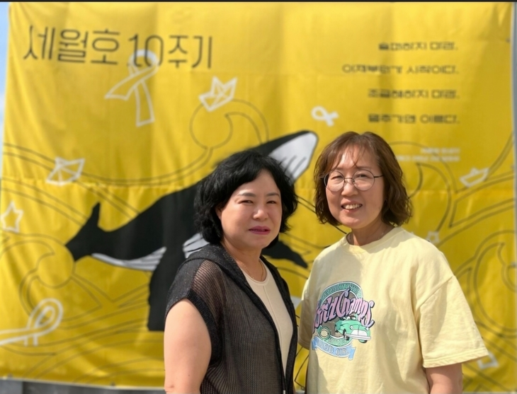 세월호 참사로 같은 학교, 같은 반 딸을 잃은 박정화(왼쪽)씨와 김순길씨가 2024년 4월 16일 경기 안산시 안산문화광장에서 열린 세월호 10주기 기억문화제 현수막 앞에 나란히 서있다. 이들은 자신들의 아픔이 되풀이되지 않도록 전국을 다니며 재난안전 교육을 펼치고 있다. 안산공동체미디어 단원FM 제공