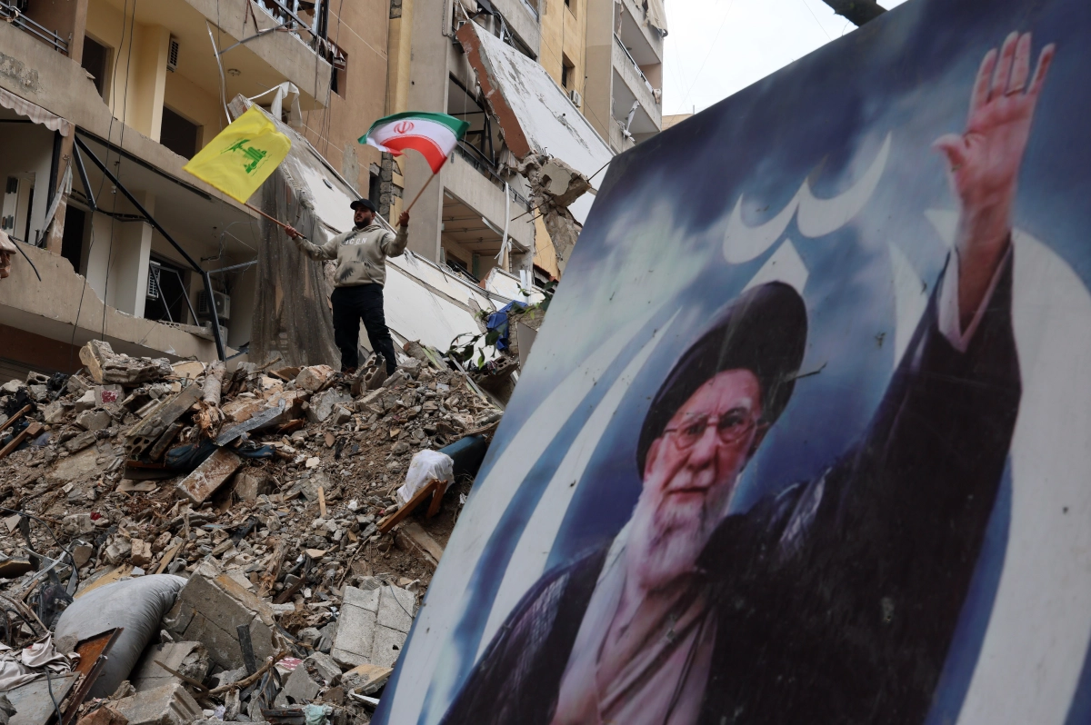 한 레바논 남성이 20일(현지시간) 이스라엘의 공습으로 파괴된 건물 잔해 위에 오른손에는 이란 국기와 왼손에는 헤즈볼라 깃발을 흔들고 있다. 그의 앞에는 이미 고인이 된 이란 최고지도자 아야톨라 알리 하메네이의 사진이 있다. 베이루트 EPA 연합뉴스
