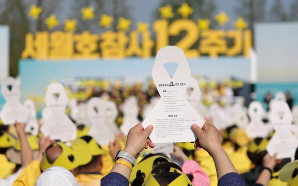 지난 16일 경기 안산시 화랑유원지에서 열린 ‘세월호 참사 12주기 기억식’에서 참석자들이 추모 리본 모양의 종이를 들고 있다.  연합뉴스