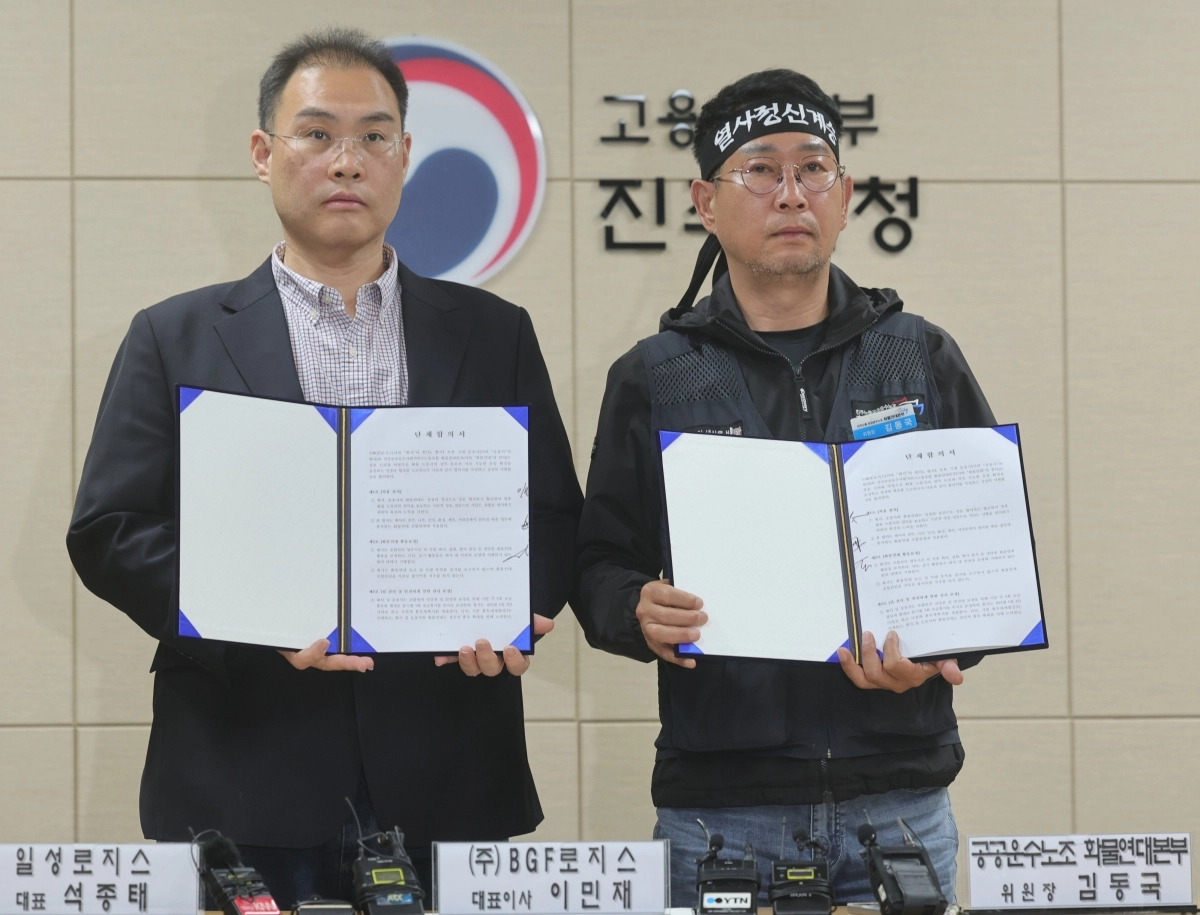 이민재(왼쪽) BGF로지스 대표와 김동국 민주노총 화물연대 위원장이 30일 고용노동부 진주지청에서 서명한 단체합의서를 들어 보이고 있다. 연합뉴스