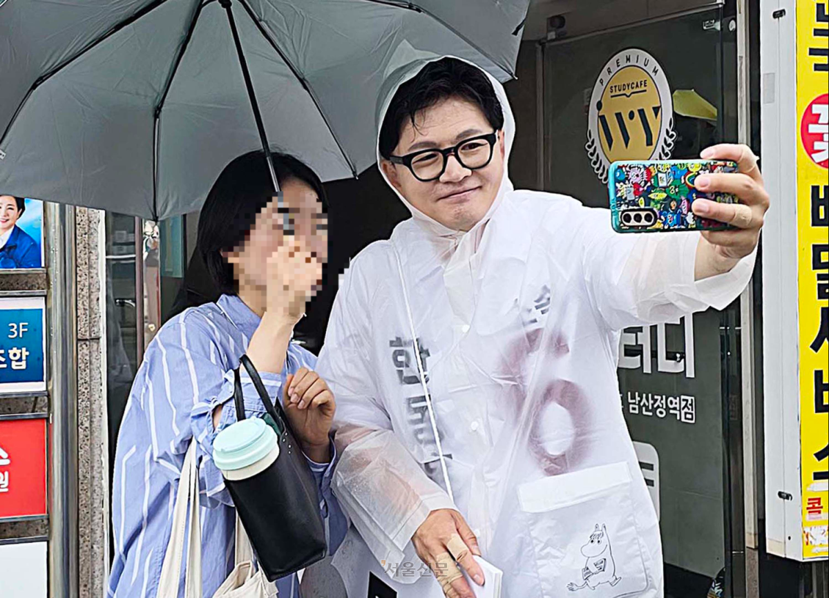 무소속으로 부산 북구갑 국회의원 보궐선거에 나선 한동훈 후보가 북구 남산정역 출구 앞에서 우비를 입고 주민과 사진을 찍고 있다.