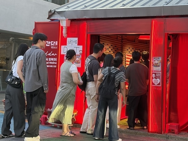 [사진: 감각적인 네온 조명 및 레드 오브제가 있는 ‘빨간다라’ 팝업 입장을 위해 줄을 선 관람객들]