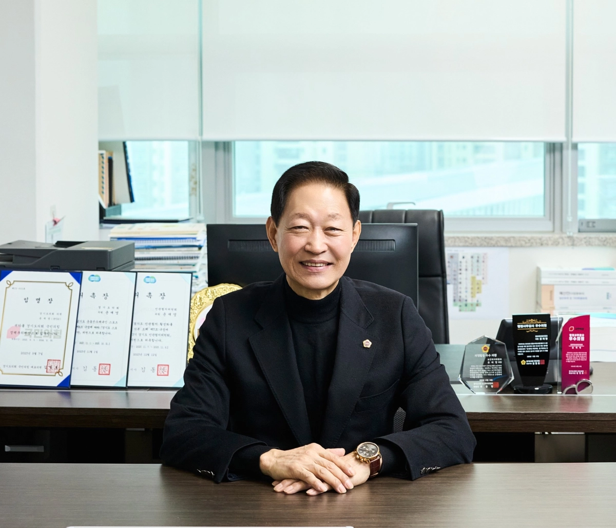▲ 윤재영 의원실 집무실에 마련된 책상에 앉아 지난 4년간의 의정활동 성과와 각종 우수의원 상패를 배경으로 기념 촬영을 하고 있다. (사진=경기도의회)