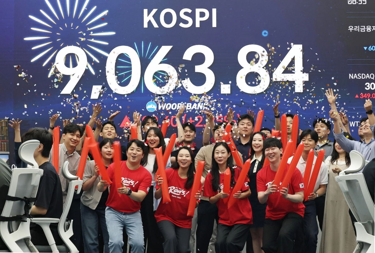 코스피 지수가 전인미답의 9000선 고지를 돌파한 18일 오후 서울 중구 우리은행 본점 딜링룸에서 직원들이 코스피 종가를 배경으로 축하 세리머니를 하고 있다. 코스피는 이날 전일 대비 199.60포인트(2.25%) 오른 9063.84에 장을 마쳤다. 2026.6.18 뉴스1