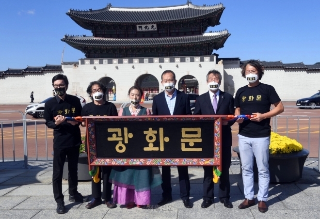 2020년 광화문 앞에서 한글 현판을 주장하는 시민단체 회원들이 훈민정음체로 적힌 현판을 들어 보이는 모습. 이들 뒤로 흰 바탕에 검정 글씨로 돼 있는 과거 광화문 현판이 보인다. 서울신문DB