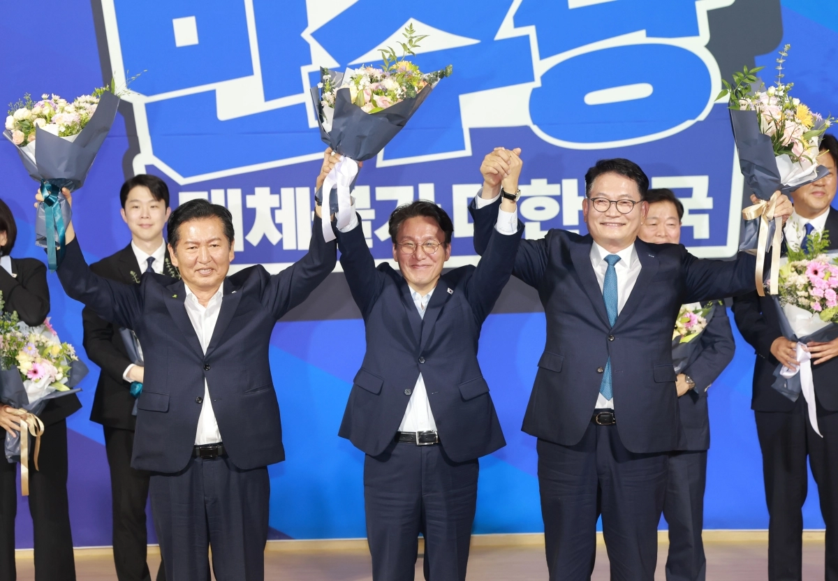 더불어민주당 8·17 전당대회 본경선에 진출한 정청래(왼쪽) 전 대표, 김민석(가운데) 전 국무총리, 송영길 의원이 23일 국회의원회관에서 열린 당대표·최고위원 예비경선 결과 발표 직후 단상에 올라 한 손에 꽃다발을 들고 기념촬영을 하고 있다. 연합뉴스