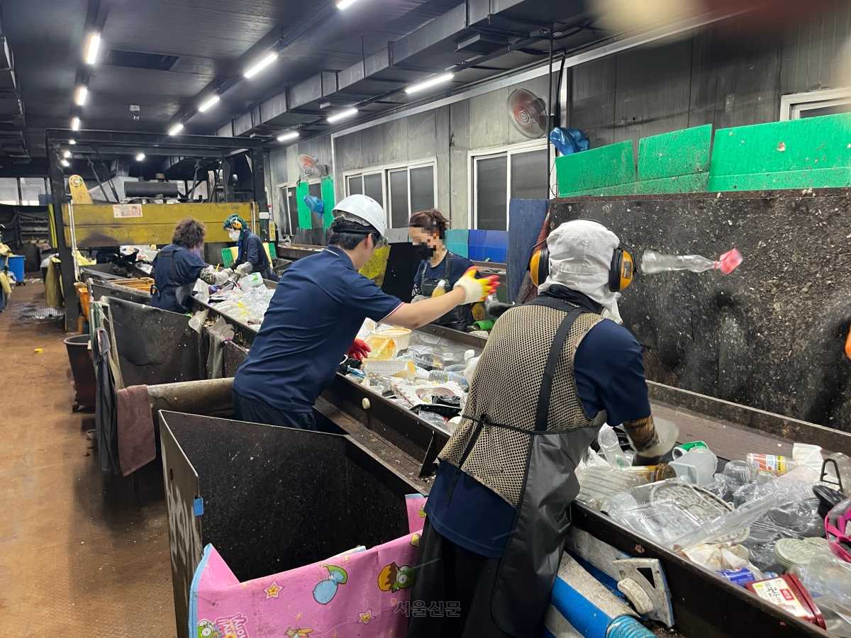 지난 3일 경기도의 한 자원재활용센터 실내 작업장에서 본지 박다운(가운데) 기자가 폐기물 더미로부터 페트병을 선별하는 작업을 하고 있다. 에어컨을 틀어도 35.6도까지 오른 찜통 현장에서 10분 만에 온몸이 땀으로 젖고, 30분이 지나자 어지럼증이 밀려왔다. 굉음을 견디기 위해 귀마개를 한 노동자(오른쪽)도 눈에 띈다. 박다운 기자