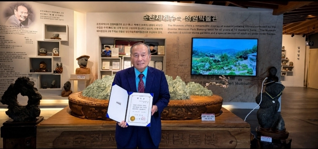 박병선 진도군 홍보대사가 순천세계수석박물관을 배경으로 위촉장을 들고 기념사진을 찍고 있다.