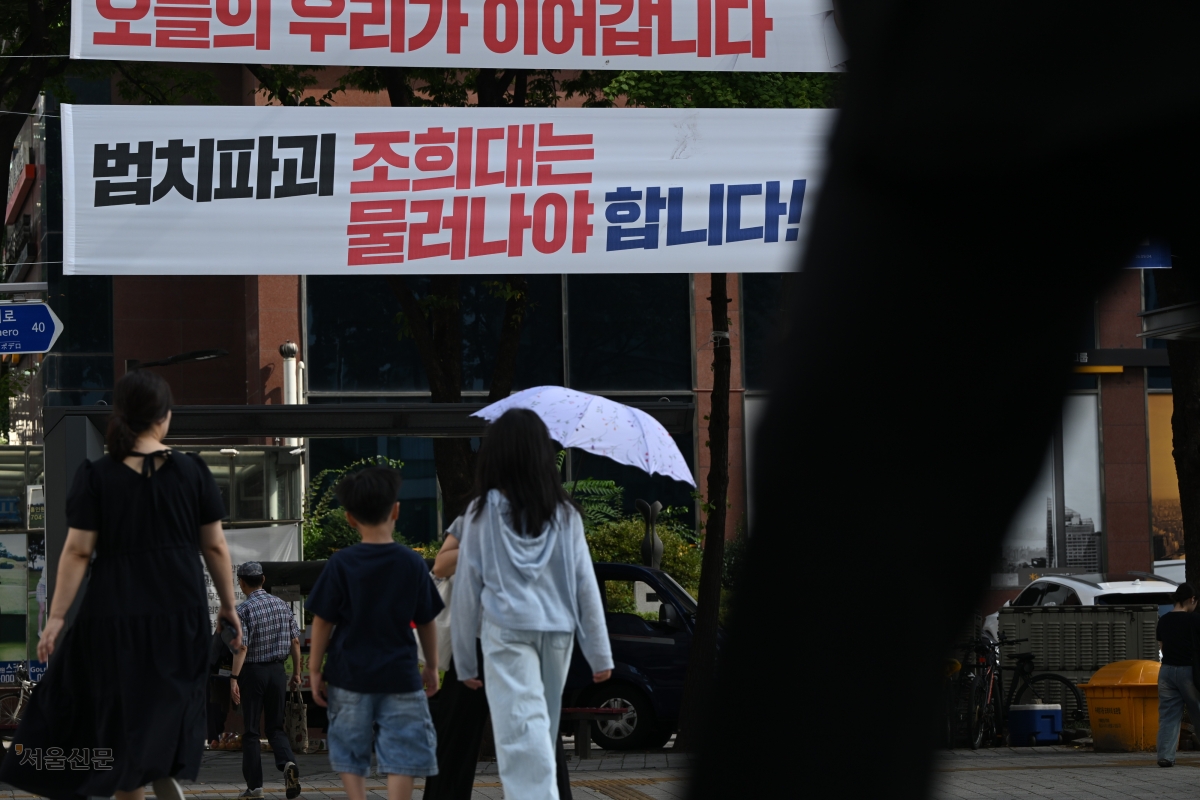 23일 서울 도심의 한 교차로 옆에 붙은 ‘법치파괴 조희대는 물러나야 합니다’는 글귀의 현수막 아래로 시민들이 지나가고 있다. 김민석 더불어민주당 대표는 지난 19일 이 같은 내용의 현수막을 전국에 걸라고 지시했다. 이지훈 기자