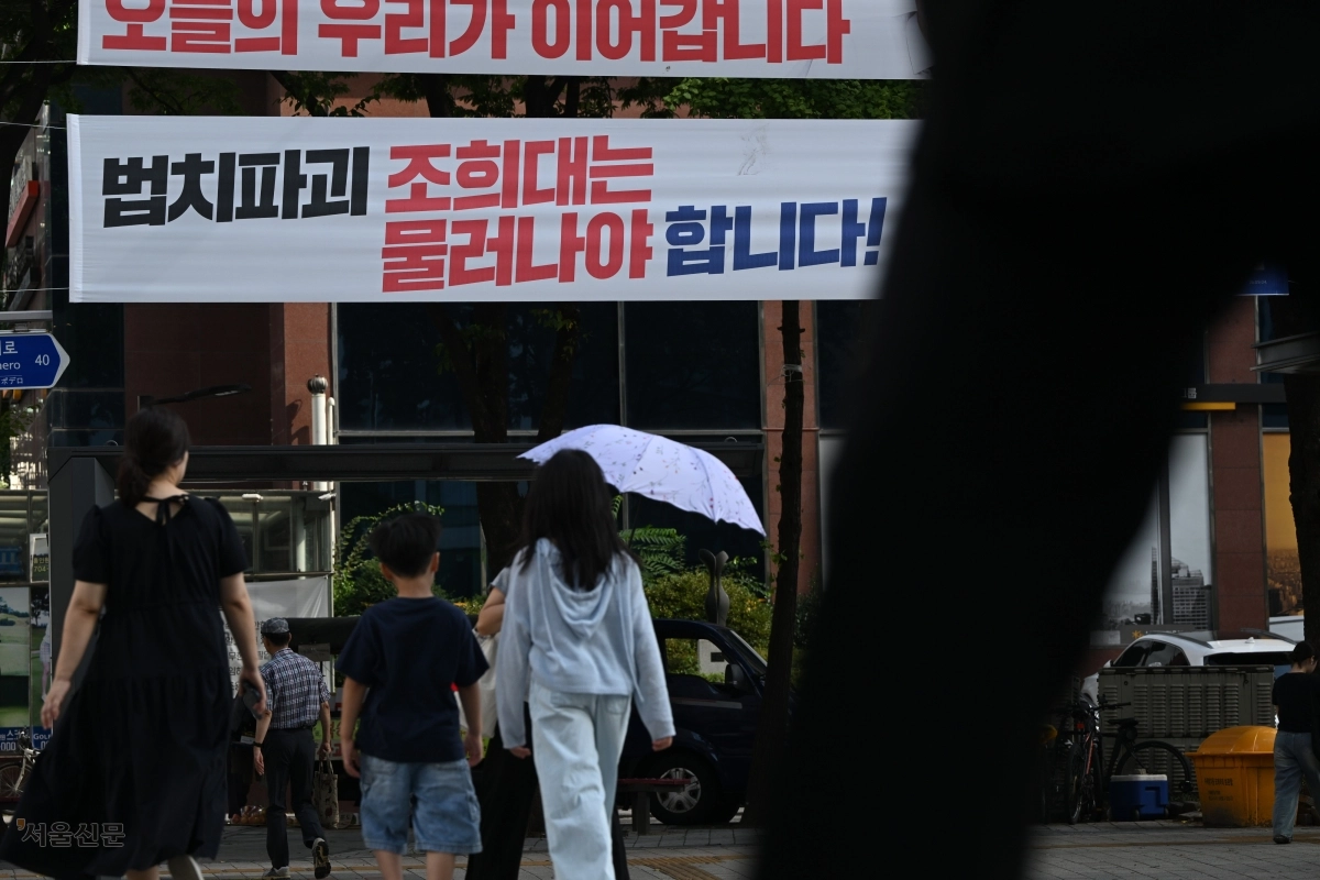 23일 서울 도심의 한 교차로 옆에 붙은 ‘법치파괴 조희대는 물러나야 합니다’는 글귀의 현수막 아래로 시민들이 지나가고 있다. 김민석 더불어민주당 대표는 지난 19일 이 같은 내용의 현수막을 전국에 걸라고 지시했다. 이지훈 기자
