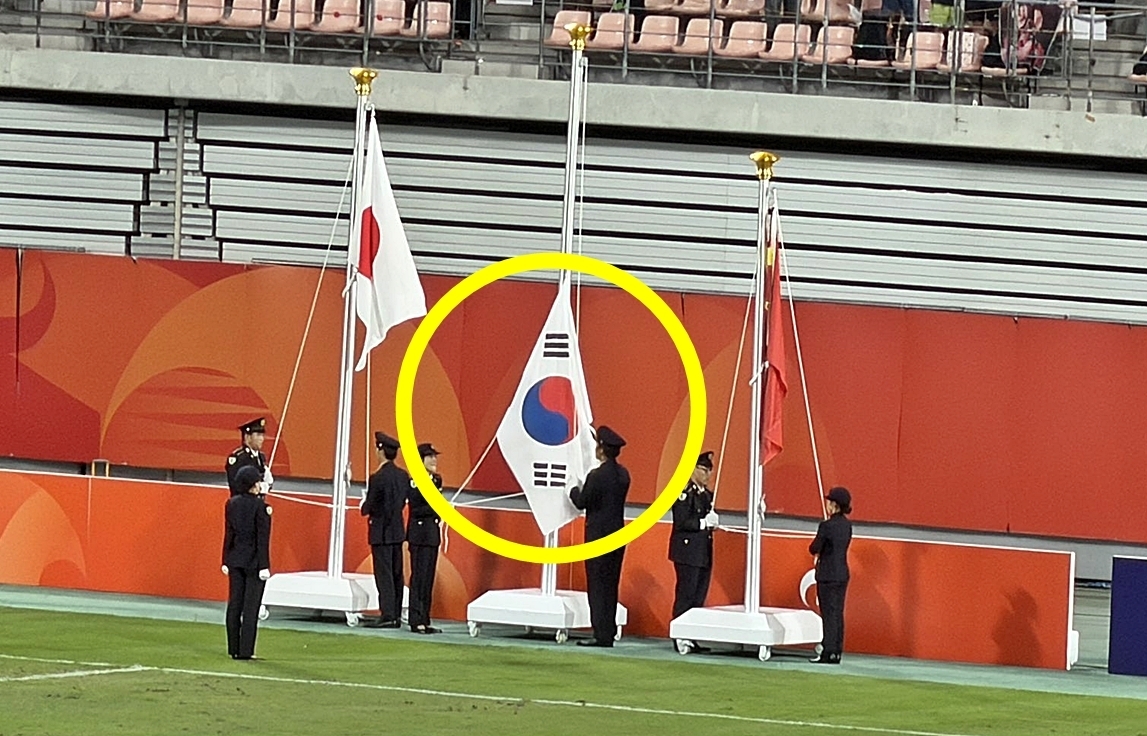 3일 이민성 감독이 이끄는 한국 23세 이하(U-23) 축구대표팀은 일본 아이치현 도요타 스타디움에서 열린 결승전에서 일본을 1-0으로 꺾고 아시안게임 최초로 남자축구 4연패를 달성했다. 하지만 선수들이 금메달을 목에 걸고 애국가를 들으며 기쁨을 누려야 할 때, 국기 게양대 가운데에 걸린 태극기가 애국가에 맞춰 제때 올라가지 않는 사고가 발생했다. 애국가가 흘러나올 때 태극기 게양을 맡은 관계자들은 뭔가 제대로 작동하지 않는 듯 허둥댔고, 이를 인지한 한국 선수들은 국기 게양대 쪽을 가리키며 당혹스러운 표정을 감추지 못했다. 결국 애국가가 끝날 때까지 태극기는 맨 위에 오르지 못했고, 관중석에선 야유가 나왔다. 일각에서는 중계 당시 화면을 증거로 제시하며 일본 측이 줄을 잡아다니는 시늉만 하는 등 일부러 태극기를 제때 게양하지 않았다는 의혹도 제기했다. 2026.10.3 엑스 캡처